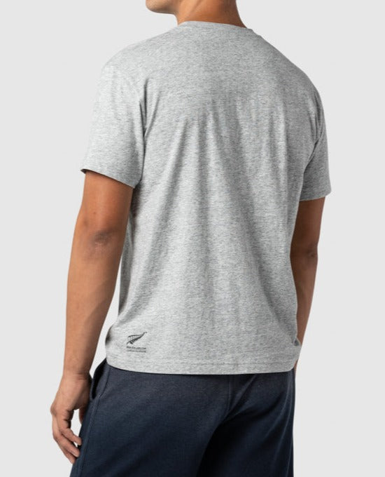 A person is standing with their back to the camera, wearing a heather gray Rodd & Gunn Cumulus Sports Fit Tee made from premium cotton and dark pants. The T-shirt features a subtle logo near the bottom on the left side. The background is plain and light gray.