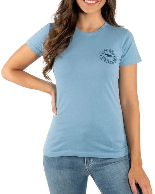 A woman is smiling and wearing the light blue Ringers Western Women's Signature Bull Classic Fitted T-Shirt, made from 100% cotton, paired with jeans. The comfortable casual T-shirt features a small logo on the left side of the chest. She is posing with one hand on her hip.