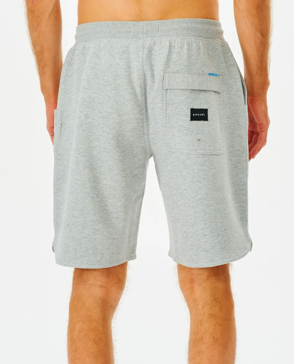A person is seen from behind wearing Rip Curl Vaporcool Shorts with a black Adidas patch on the right pocket. The gray shorts, featuring an elastic waistband, fall to mid-thigh against a plain white background.