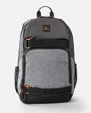 The Rip Curl Fader 28L Hydro Backpack boasts a grey and black design with a top handle, two main zippered compartments, a dedicated padded laptop section, a small front pocket with orange zipper pulls, side mesh pockets, and a breathable airmesh back panel for comfort.