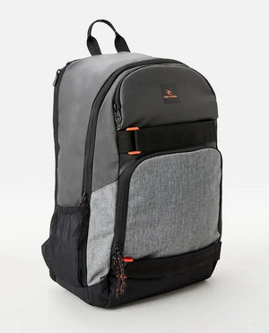 The Rip Curl Fader 28L Hydro Backpack is gray and black with multiple compartments and orange accents. The top section showcases a logo featuring a stylized wave along with the brand name "Off Coast." It includes a dedicated padded laptop compartment, a zippered front pocket, side mesh pockets, and a breathable airmesh back panel.