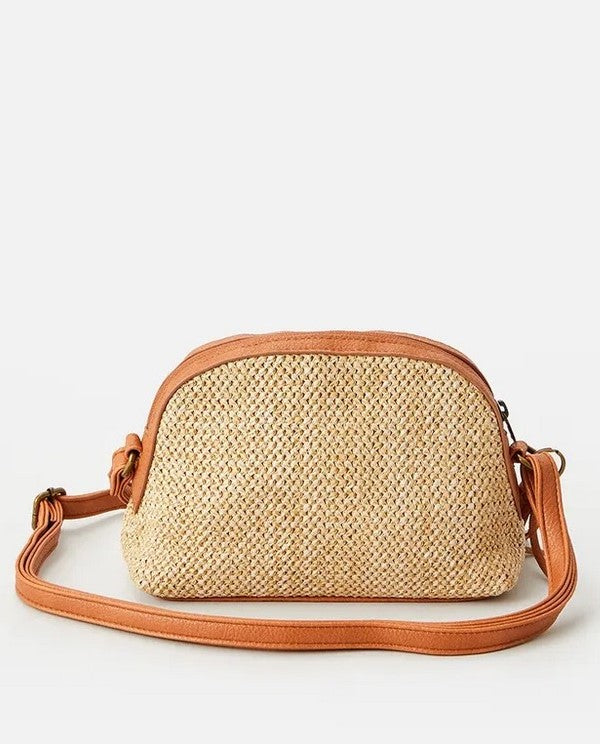 The Rip Curl Surf Gypsy Cross Body Bag has a woven straw texture with tan leather accents on the base and top. It includes an adjustable shoulder strap, a detachable tassel keyring, and is set against a plain white background.