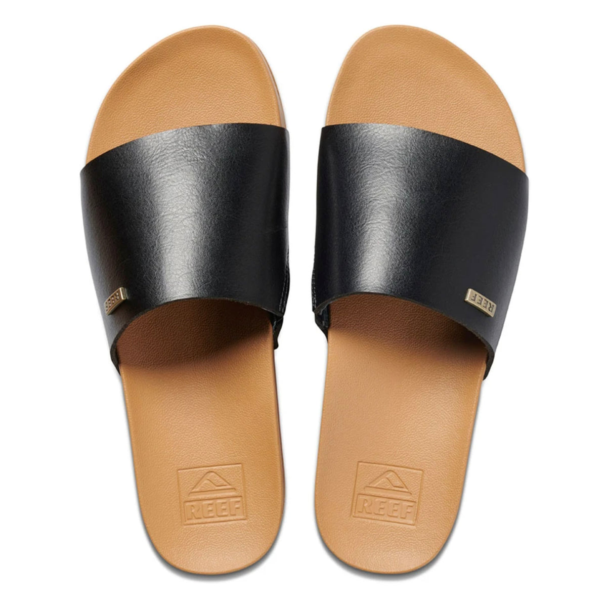 A pair of REEF Cushion Scout slides in brown and black, featuring a single wide black vegan leather strap over the foot. The tan footbed showcases the "Reef" brand logo embossed near the heel and includes a cushion bounce midsole for added comfort. Each strap is adorned with a small metallic "Reef" tag, photographed from above.