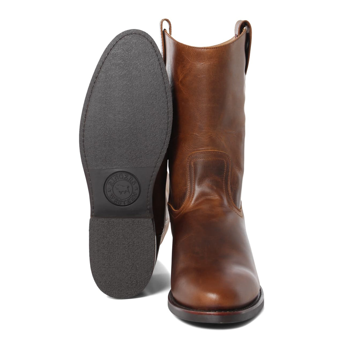 A pair of brown genuine leather cowboy boots are displayed. One Ringers Western Kimberley High Boot stands upright, showcasing its smooth, vintage finish, while the other is placed sole-forward, highlighting the brand's logo embossed on the heel's rubber sole.