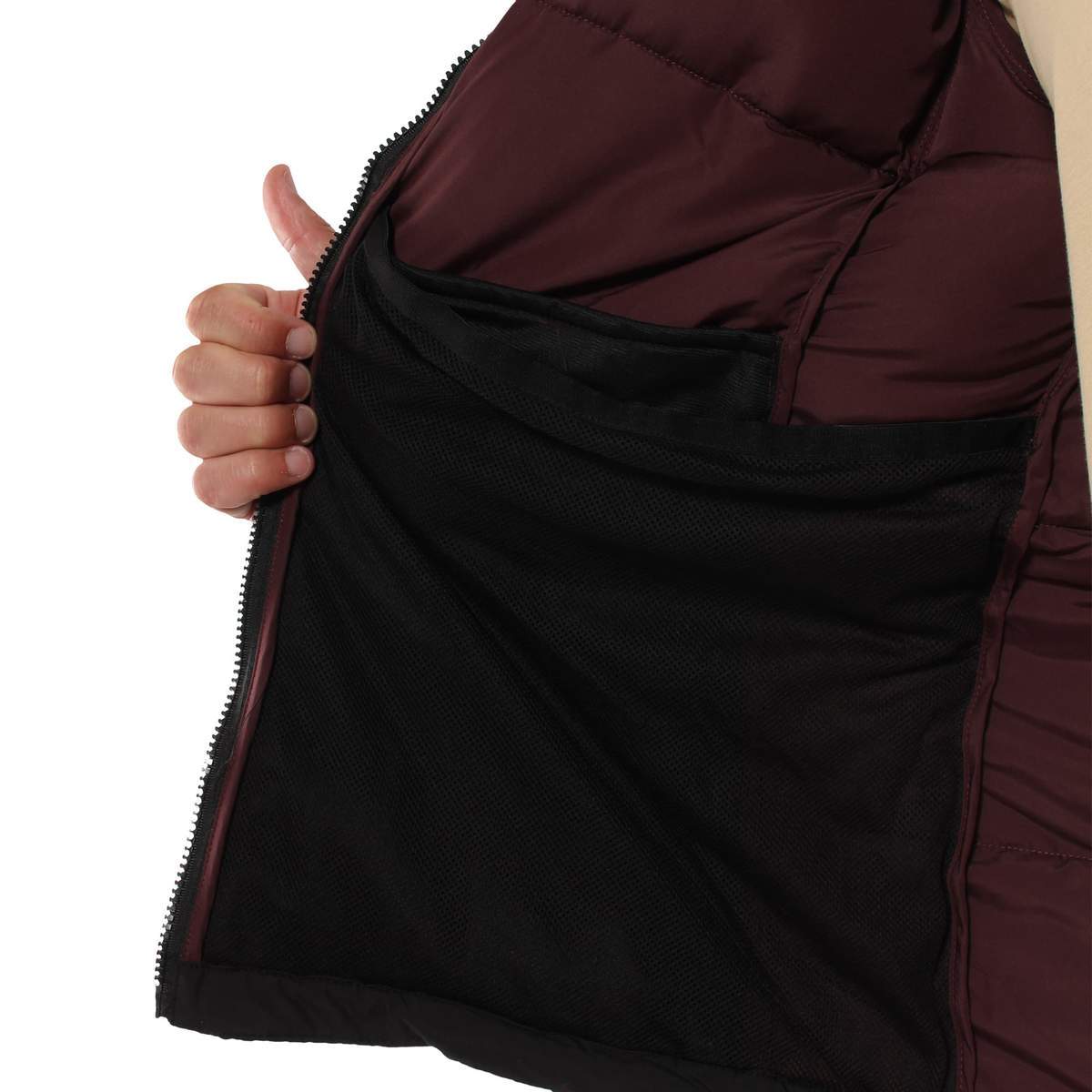 Close-up of a person holding open a burgundy Ringers Western Bairnsdale Puffer Jacket, revealing its black, mesh inner pocket. The hand is positioned to give a clear view of the pocket's size and placement. A beige garment is partially visible on the person's other side.