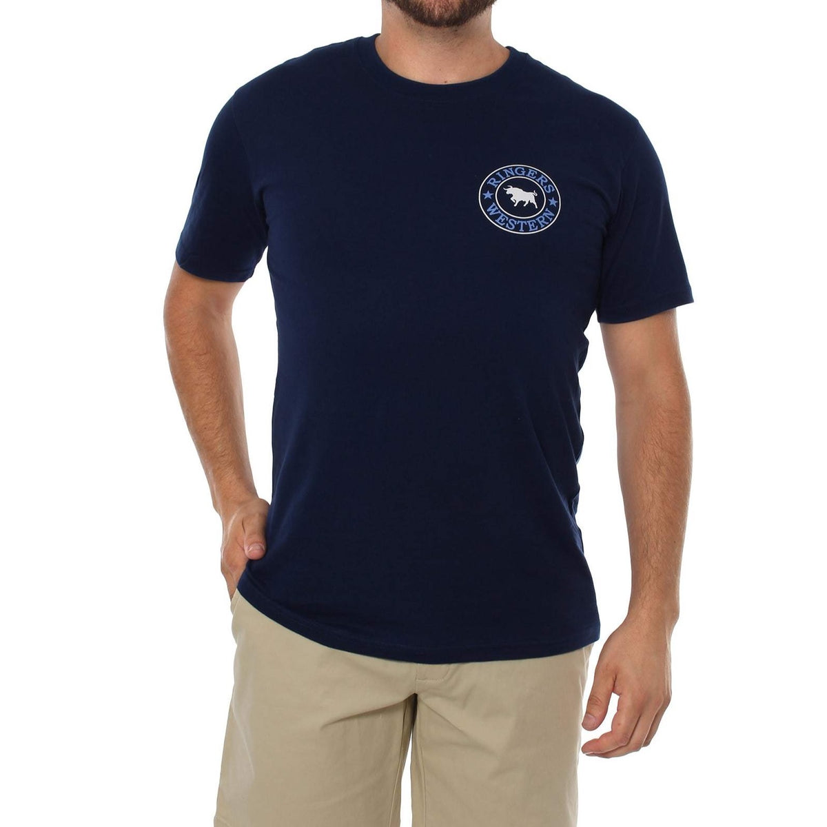 A man with short brown hair wearing a navy blue, crew neck Ringers Western Signature Bull Classic T-Shirt featuring a white circular logo with a bull on the left side of the chest. He has his left hand in his beige shorts pocket and stands against a plain white background.
