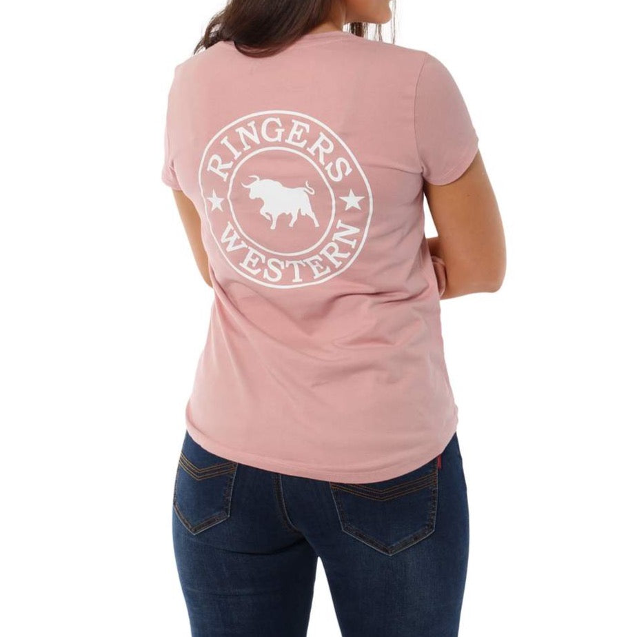 A woman wears the Ringers Western Signature Bull Relaxed V-Neck T-Shirt in light pink, made from 100% cotton with a white circular logo and bull graphic on the back, paired with dark blue jeans and standing with her back to the camera.