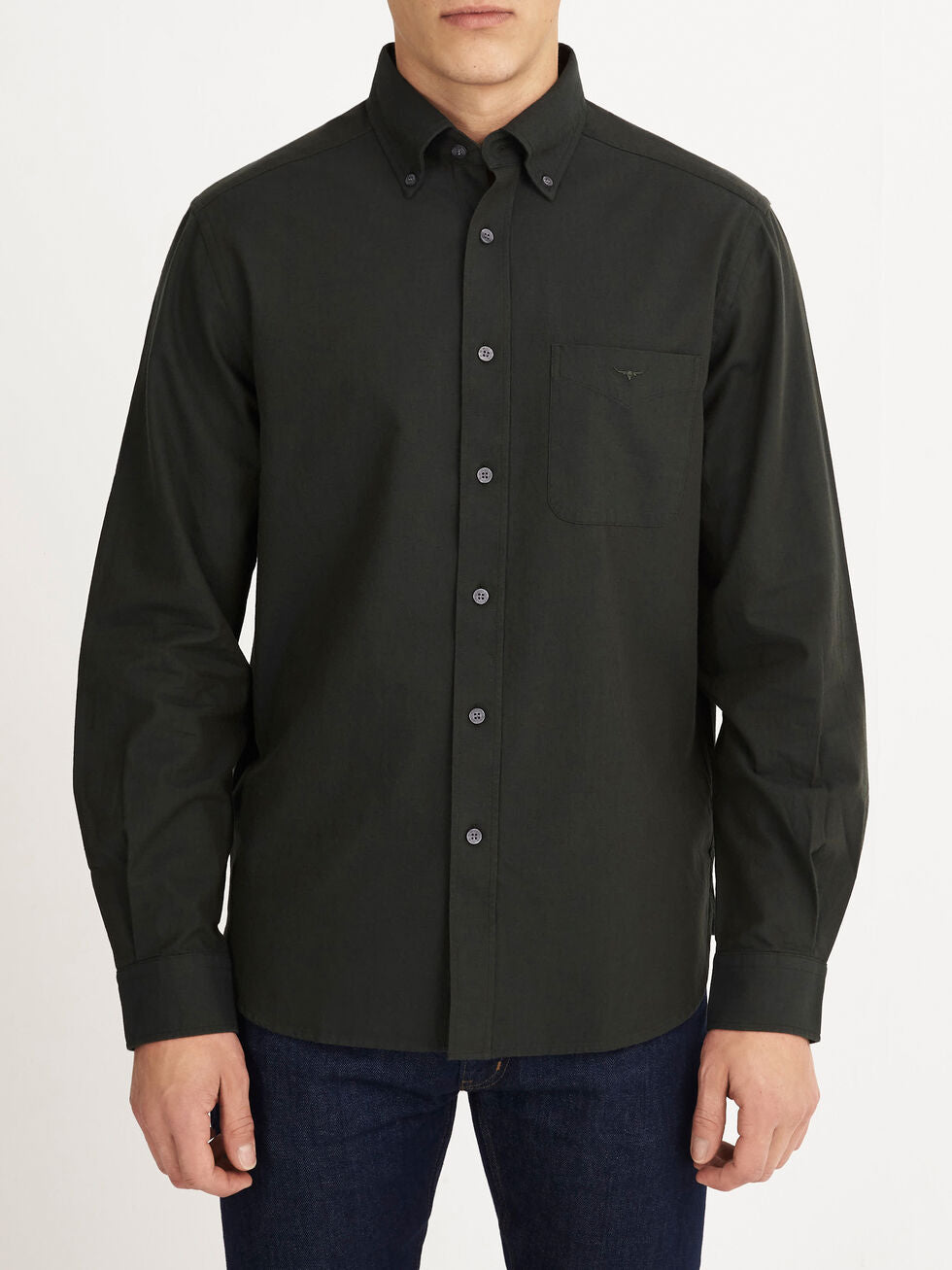 A man wearing an RM Williams Collins Shirt in dark green with long sleeves and a chest pocket, paired with blue jeans, stands against a plain white background.