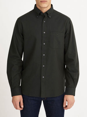 A man wearing an RM Williams Collins Shirt in dark green with long sleeves and a chest pocket, paired with blue jeans, stands against a plain white background.
