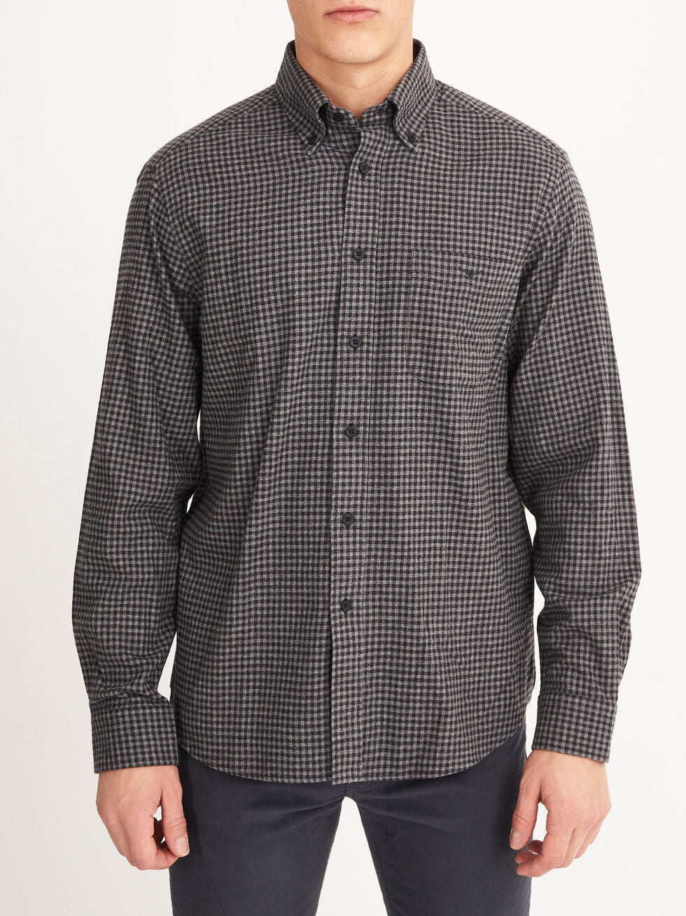 A person wears the RM Williams Collins Shirt, a long-sleeved, button-up shirt in black and gray small checkered brushed cotton, paired with dark pants and standing against a plain white background.