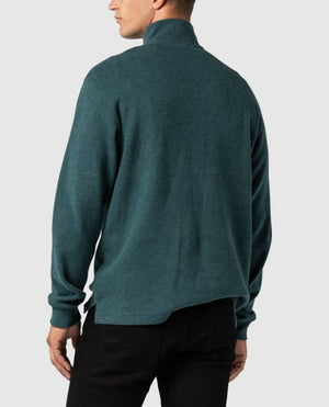 A person stands facing away, dressed in a stylish Rodd & Gunn Alton Ave Sweat in teal and black pants. The background is plain grey. The comfortable sweater has a relaxed fit and appears to be made of soft, knit material. The person’s head is turned slightly to the right.