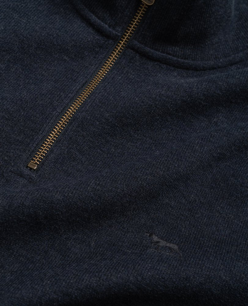 Close-up of a Rodd & Gunn Alton Ave Sweat, a dark blue 100% cotton half zip sweater with a gold zipper slightly open at the collar and a subtle embroidered kangaroo logo near the bottom right.