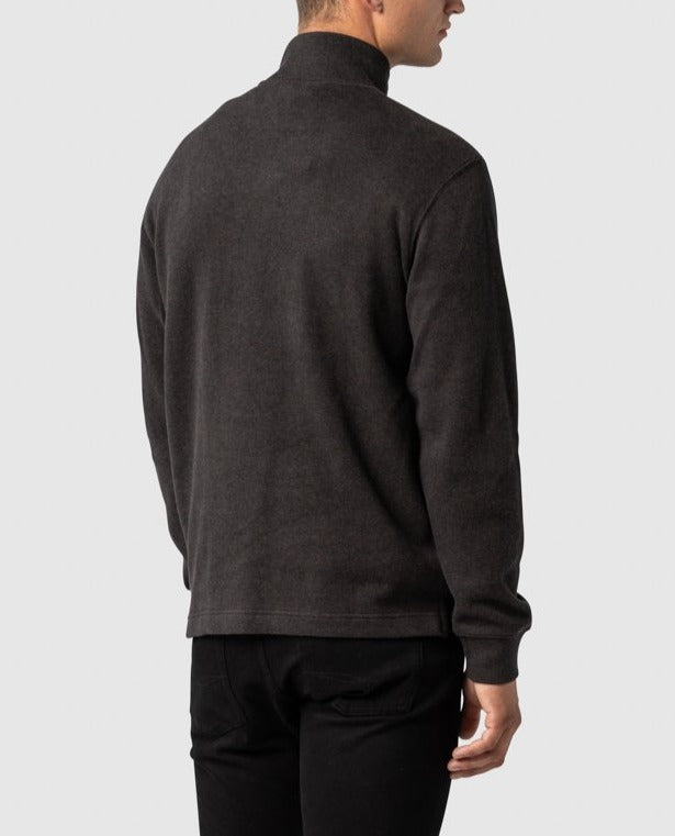 A man is standing with his back to the camera, wearing a relaxed fit Rodd & Gunn Alton Ave Sweat and black pants. He has short hair and is looking slightly to the side against a plain, light-colored background.