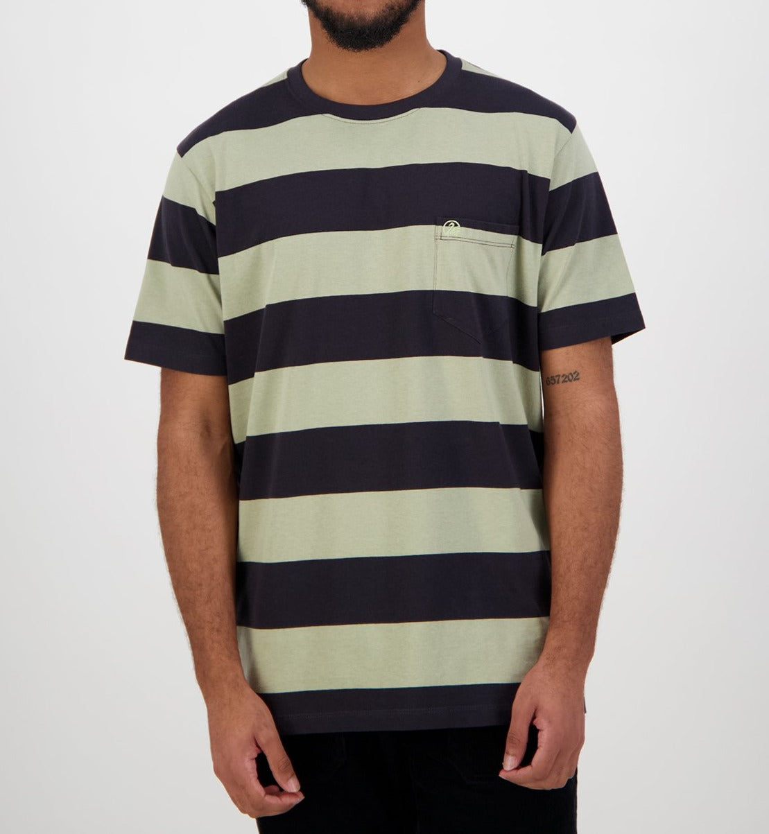 A man wearing a Swanndri Tomarata Stripe Tee, featuring wide horizontal olive green and black stripes, 100% cotton fabric, and a small chest pocket, stands against a plain background.