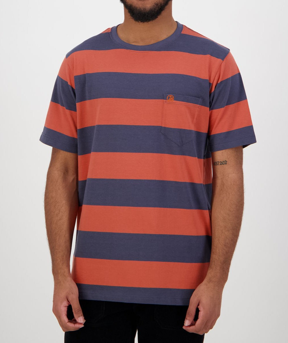 A man models a Swanndri Tomarata Stripe Tee, made from 100% cotton, with bold orange and dark blue horizontal stripes and a small chest pocket, set against a plain white background.
