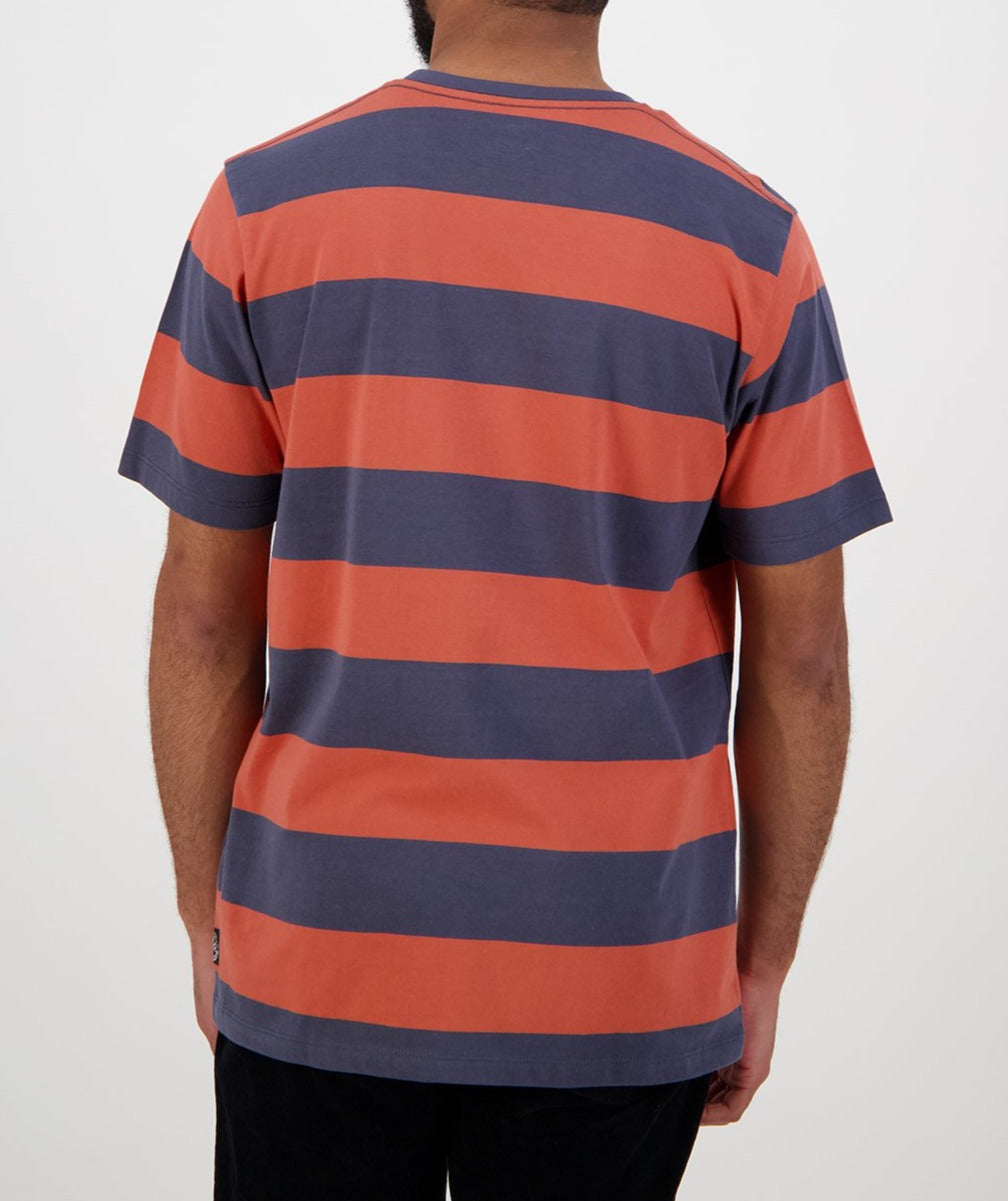 Seen from the back, a person wears the Swanndri Tomarata Stripe Tee, a casual 100% cotton shirt with wide horizontal orange and dark gray stripes and short sleeves, set against a plain white background.