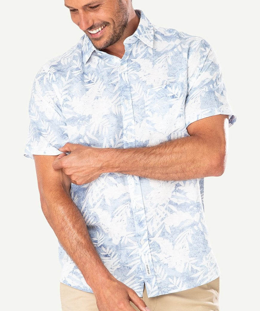 A man smiles and looks down while wearing the Gazman Linen Blend Palm Print Shirt in blue, paired with light-colored pants.