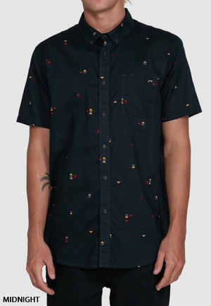 Someone wearing the Billabong Sundays Mini Shirt in Midnight—a short-sleeve, button-up casual shirt with a colorful geometric print and chest pocket—stands against a light gray background.