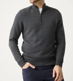 A man wears the Toorallie Grafton Half Zip Knit in dark gray over a white shirt and navy blue pants, standing with one hand in his pocket against a plain white background. His face is partially out of frame.