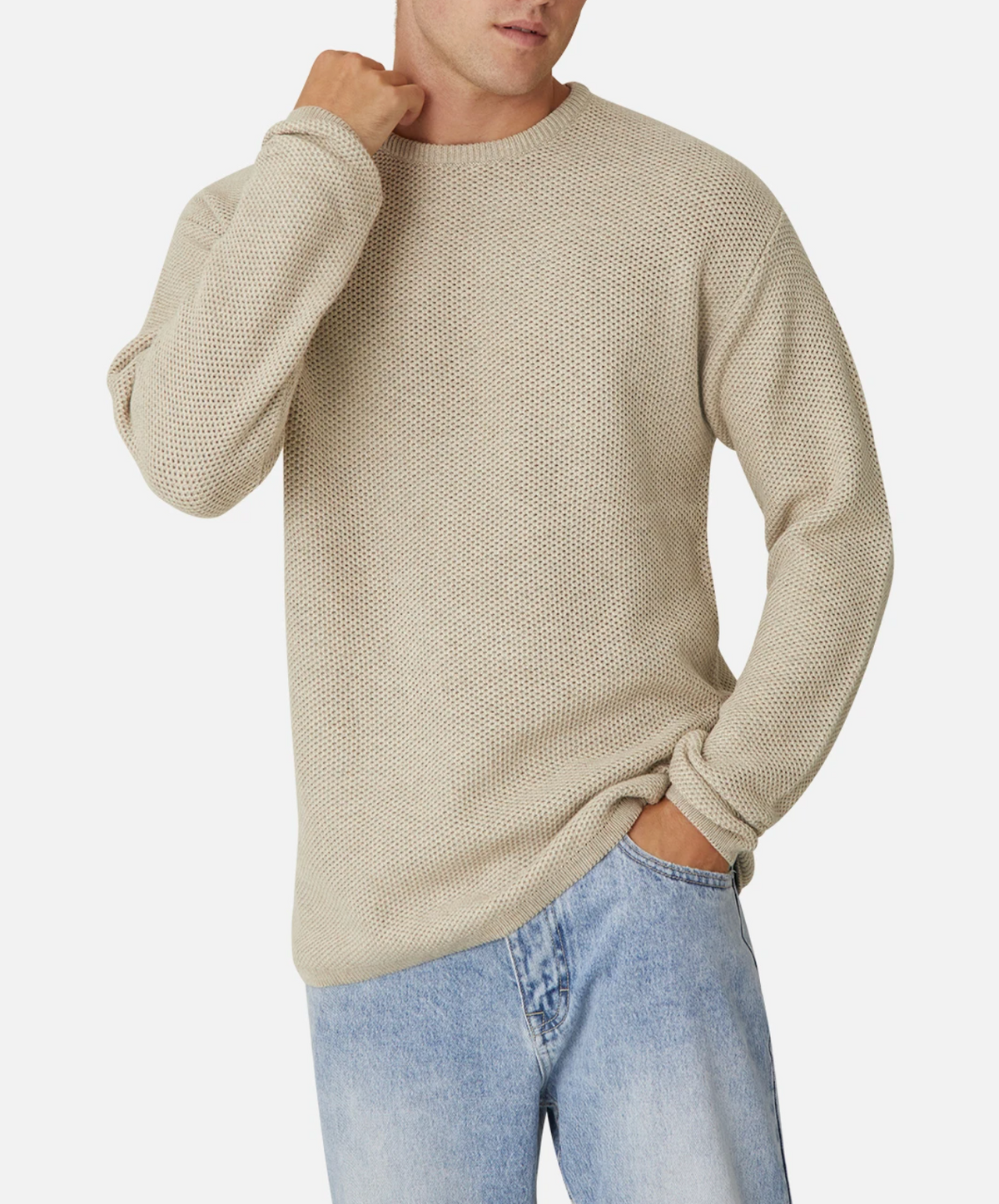 A person wearing the Industrie The Washed Culver Knit, a 100% cotton beige sweater, and light blue jeans stands against a white background. The individual has one hand in their pocket and the other adjusting the collar of the stylish knit sweater. The outfit appears casual and relaxed.