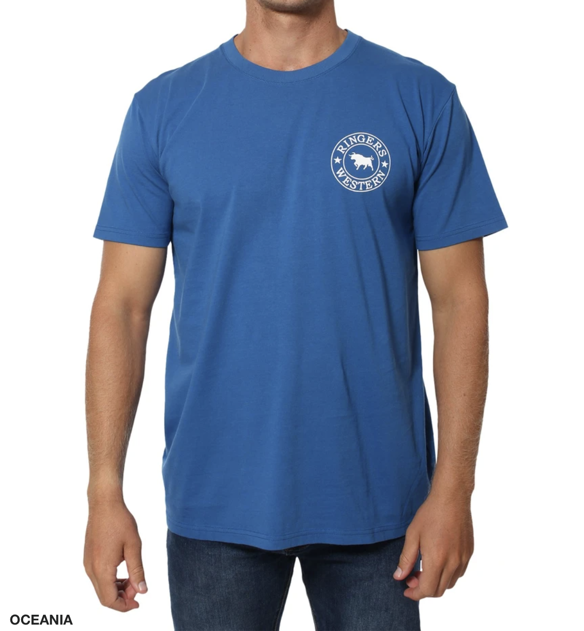 Someone is wearing the Ringers Western Signature Bull Classic T-Shirt, a blue short sleeve likely made of 100% cotton, featuring a circular logo with text and a graphic on the left chest. They're also in dark jeans against a plain white backdrop.