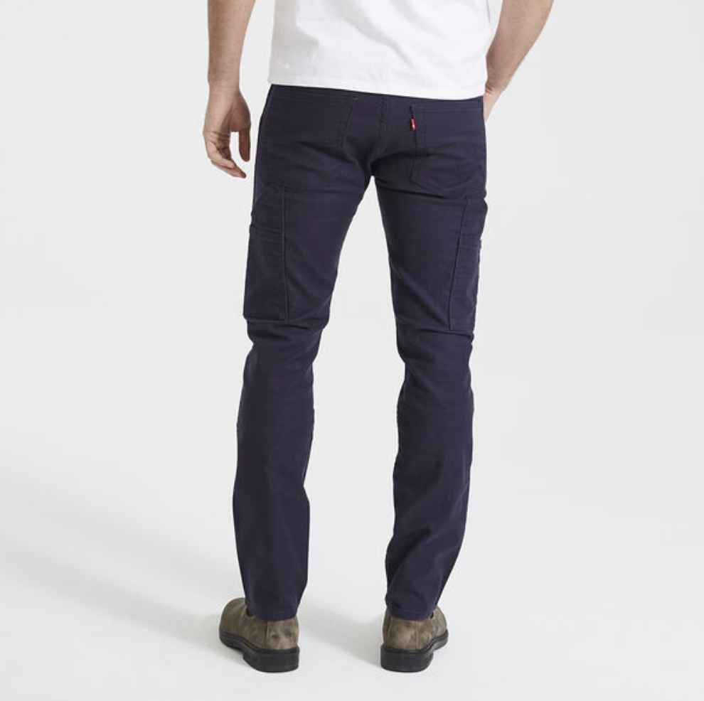 A person is standing, facing away from the camera, wearing a white shirt, Levis Workwear 511 Utility Pants in dark navy blue, and comfortable brown shoes. The background is plain white.