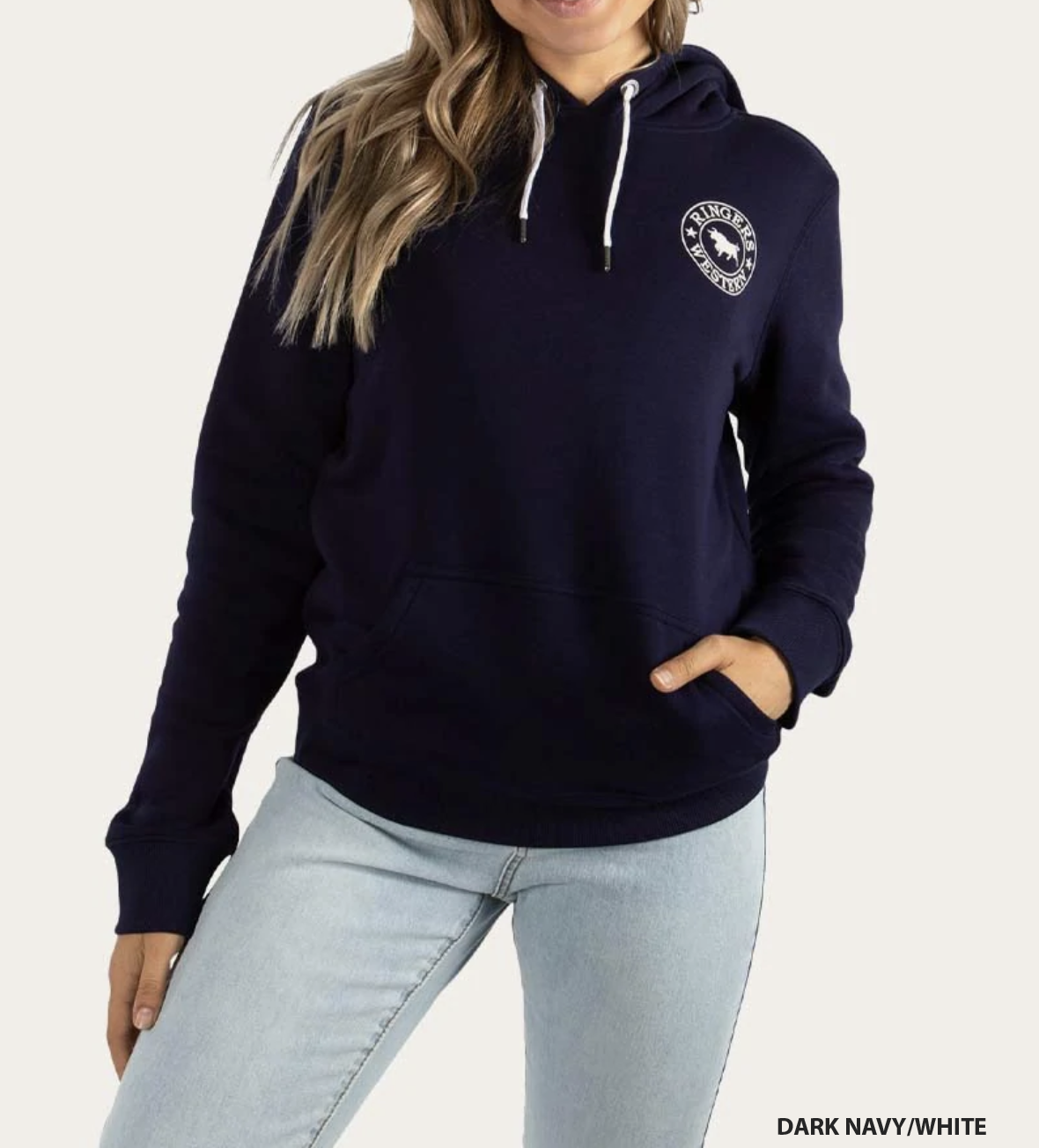 A person with long hair is wearing a casual, comfortable Ringers Western Womens Signature Bull Hoodie in dark navy, which features a small circular logo on the chest and white drawstrings. They are also wearing light blue jeans and have one hand in the hoodie pocket. The text "DARK NAVY/WHITE" is at the bottom-right corner of the hoodie.