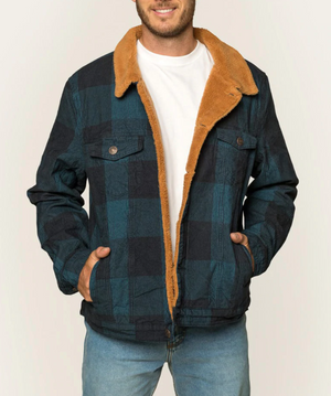 A person wears the Ringers Western Milawa Corduroy Jacket, featuring a blue and black checkered pattern with a brown fur-lined collar. The stylish jacket is paired with a white T-shirt and light blue jeans. Hands are tucked casually in the pockets of the comfortable jacket, set against a plain light-colored background.