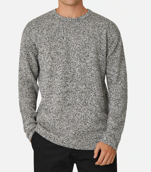 A person wearing the comfortable Industrie The Hacienda Knit, featuring a gray and white speckled design, relaxed fit, and round neckline, pairs it with black pants while standing against a plain white background, one hand in their pant pocket.