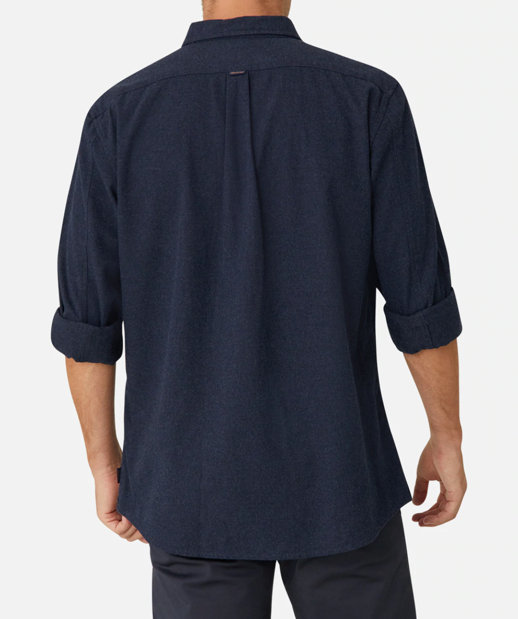 An individual is seen from behind wearing an Industrie The Taylor Shirt, a dark blue long-sleeve design with the sleeves casually rolled up to the elbows. This comfortable and casual shirt, made of 100% cotton, features a pleat down the center of the back. They are also wearing dark pants against a plain white background.