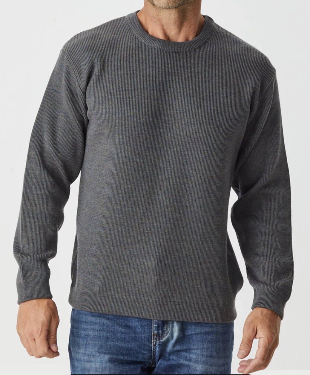 A person in a dark gray Aklanda Fishermans Rib Crew Pullover and blue jeans stands against a plain white background. The Merino wool pullover features a ribbed texture and crew neck. The person's head is cropped from the image.