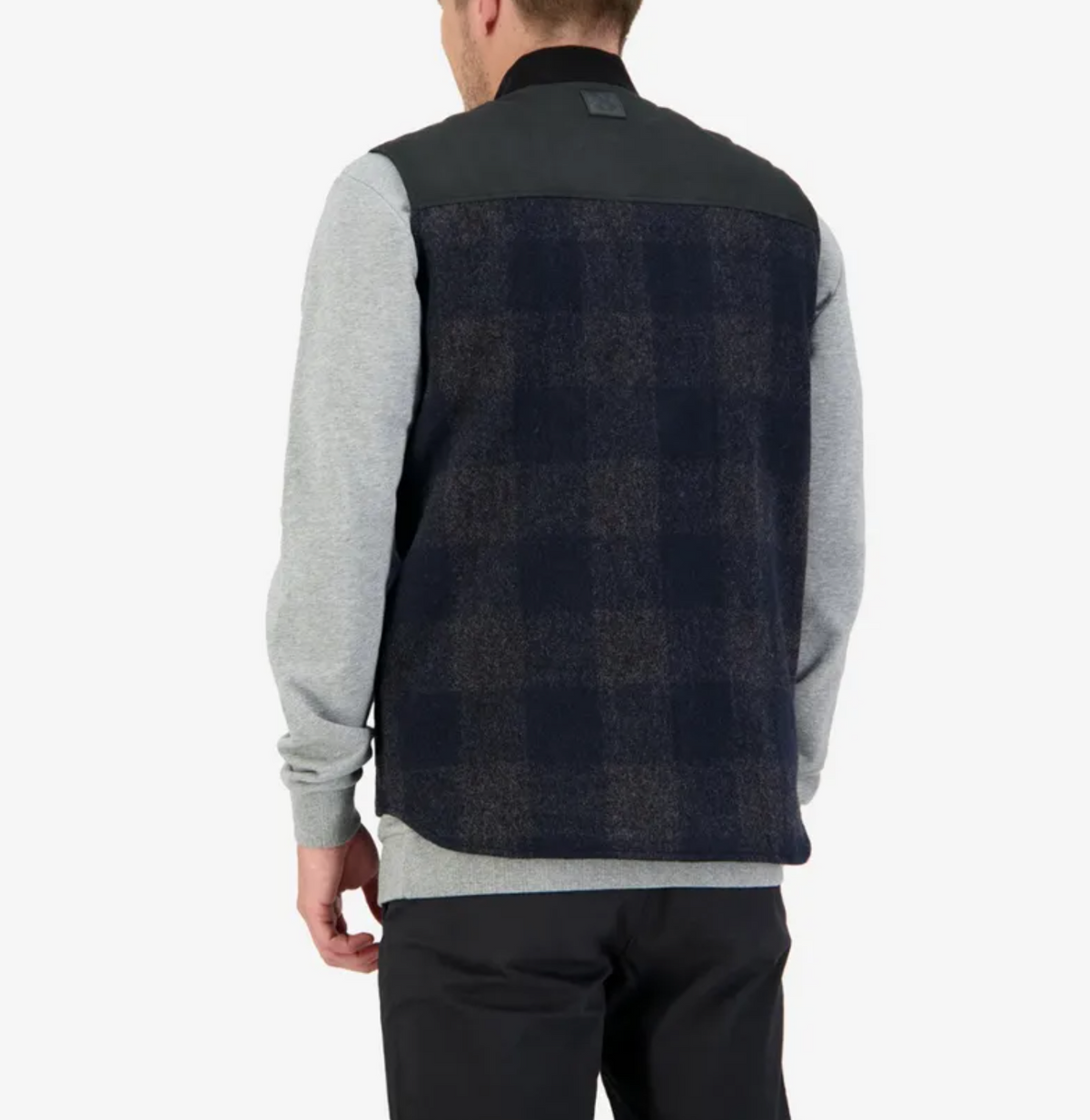 A person is seen from behind wearing the Swanndri West Melton Wool Vest, featuring a dark plaid pattern and quilted lining, over a grey sweatshirt. They stand against a plain white background, complemented by dark pants.