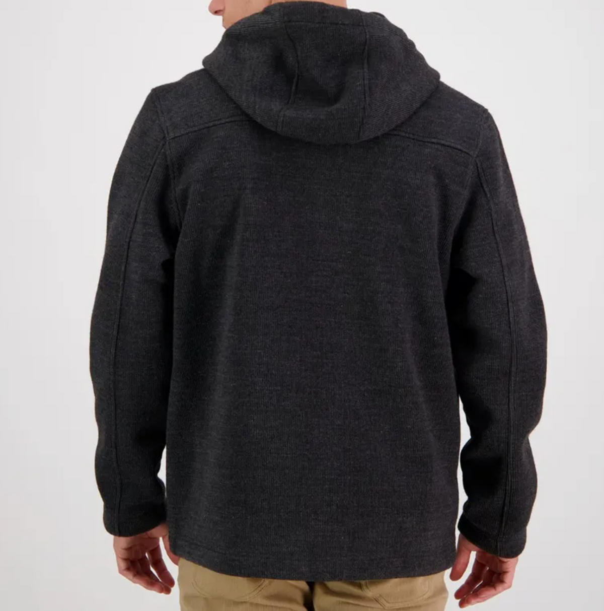 A person wearing the Swanndri Rifleman Wool Blend Hoody in dark gray, with visible seams and a water-resistant finish, is shown from behind. They pair it with light-colored pants, ready for any weather against a plain light background.