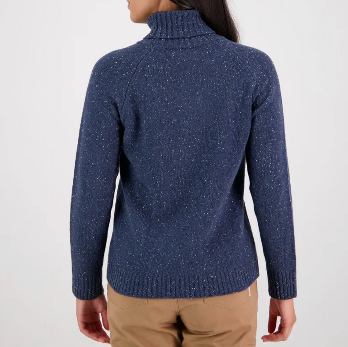 A person with long dark hair is shown from the back, wearing a stylish Swanndri Lyttleton Roll Neck Jumper in blue speckled lambswool and beige pants against a plain white background. The jumper features a ribbed collar, cuffs, and hem.