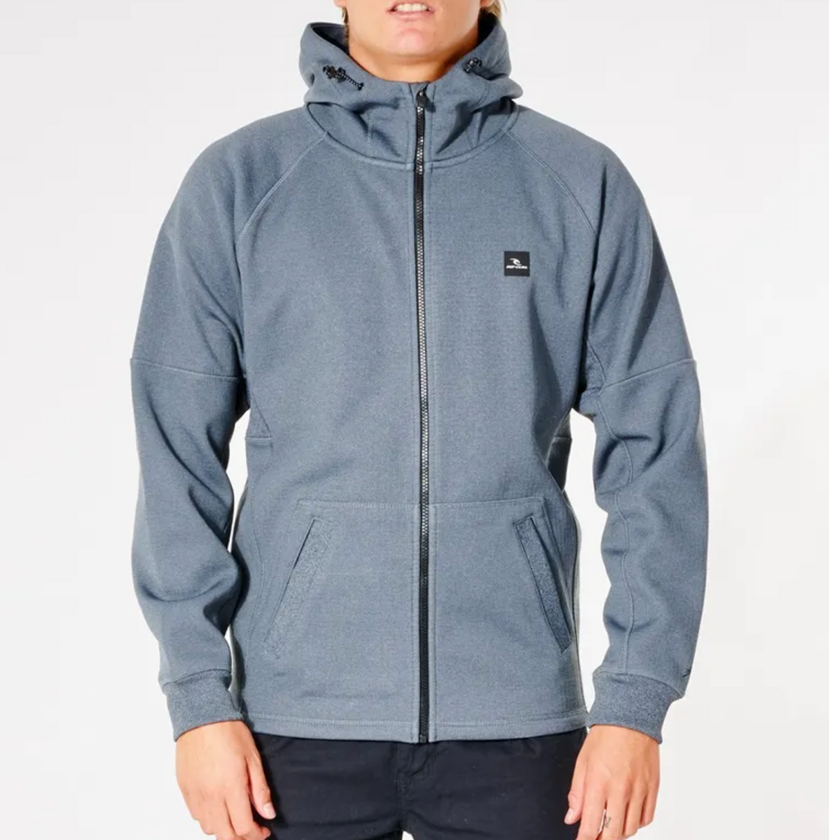 A person wearing the Rip Curl Anti Series Storm Zip Thru, a gray long-sleeve zip-up hoodie with a hood and two front pockets. The hoodie features Durable Water Resistant protection and a small black rectangular logo on the left chest. The person is standing against a plain white background.