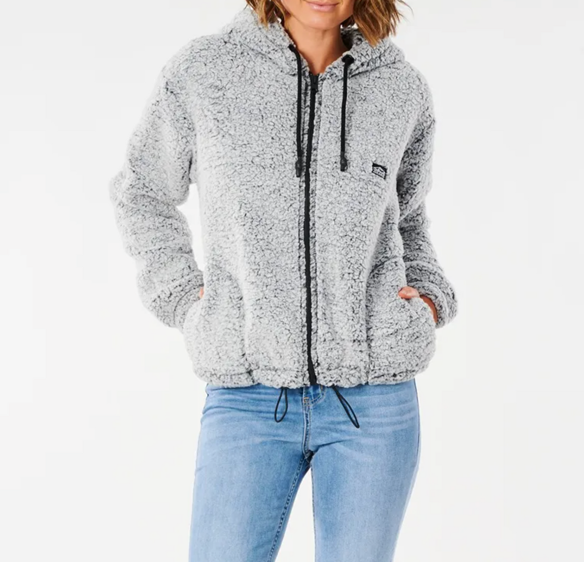 A person wearing a Rip Curl Dark N Stormy Zip Thru hoodie, which is light gray with black drawstrings and made of poly marble fleece. The hoodie features a hood and front pockets where the person has their hands. They are dressed in light blue jeans against a plain white background.