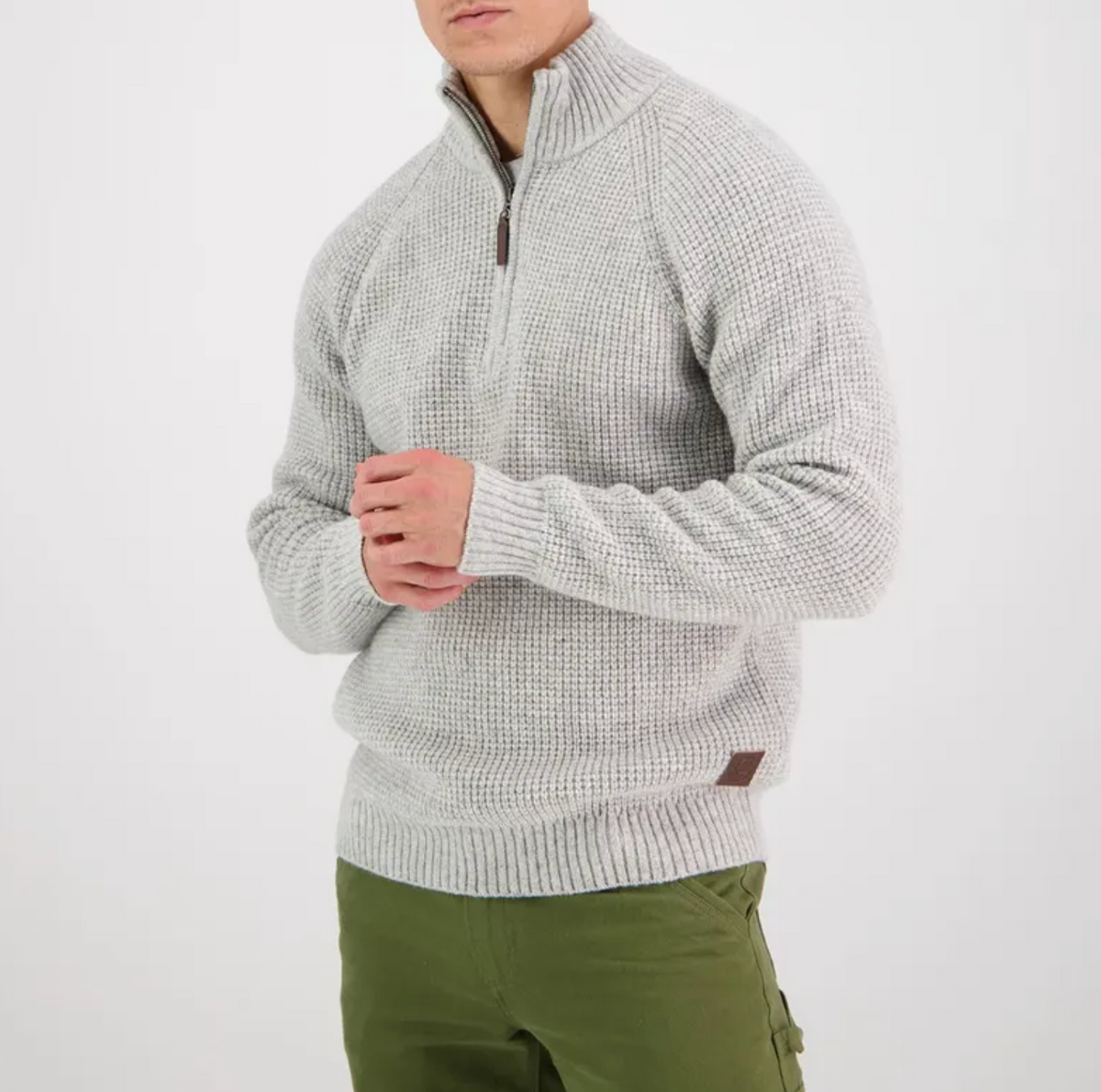 A person in a Swanndri Chalky Island Waffle Jumper, a light gray long-sleeved sweater with a quarter zip made from lambswool knit, stands against a white background. They're also wearing green cargo pants; their face is not visible.