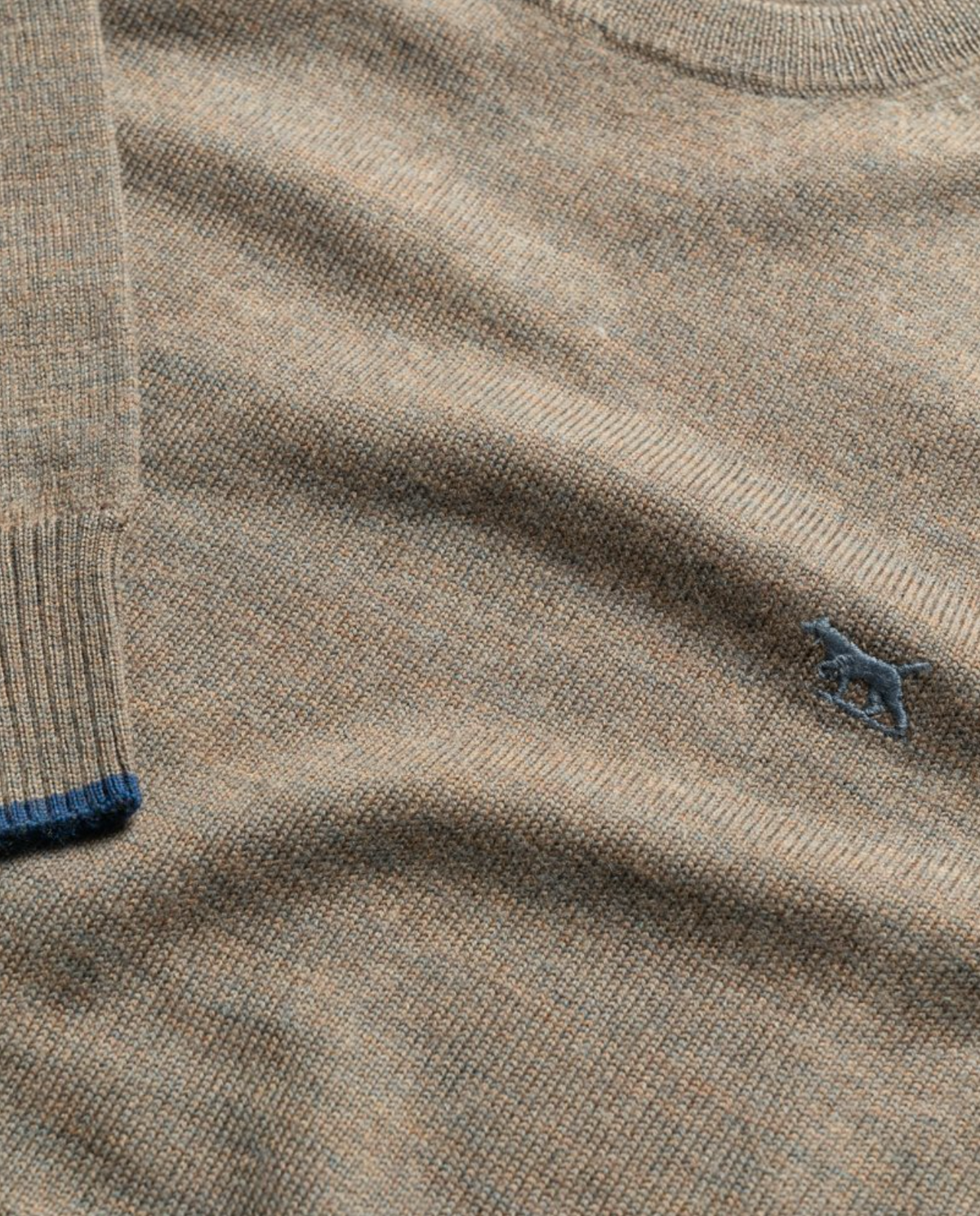 A close-up of the Rodd & Gunn Abberfield Knit, a brown textured sweater made from luxurious Australian Merino Wool, shows the iconic blue horse logo on the chest and refined blue knit cuffs at the sleeve's end.