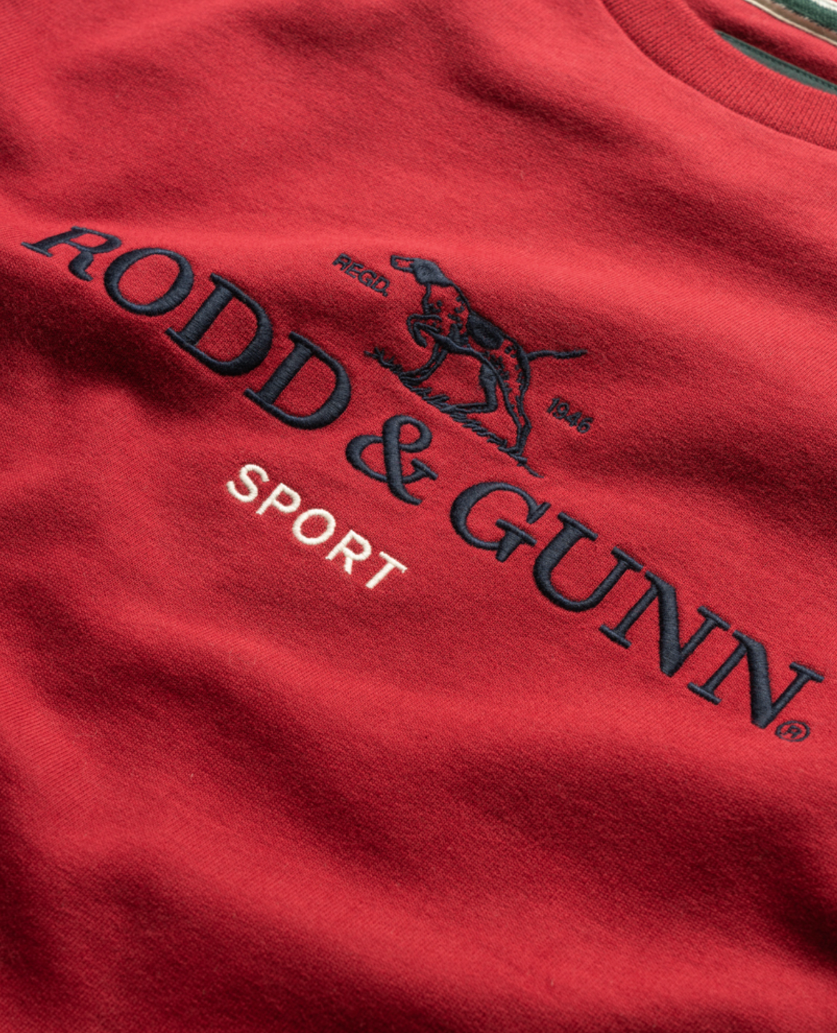 The Rodd & Gunn Grenada North Sweat is a 100% cotton crew neck sweatshirt featuring "RODD & GUNN" in bold navy letters with "SPORT" below in white, and an elegant embroidery of a dog silhouette above the text for added sophistication.