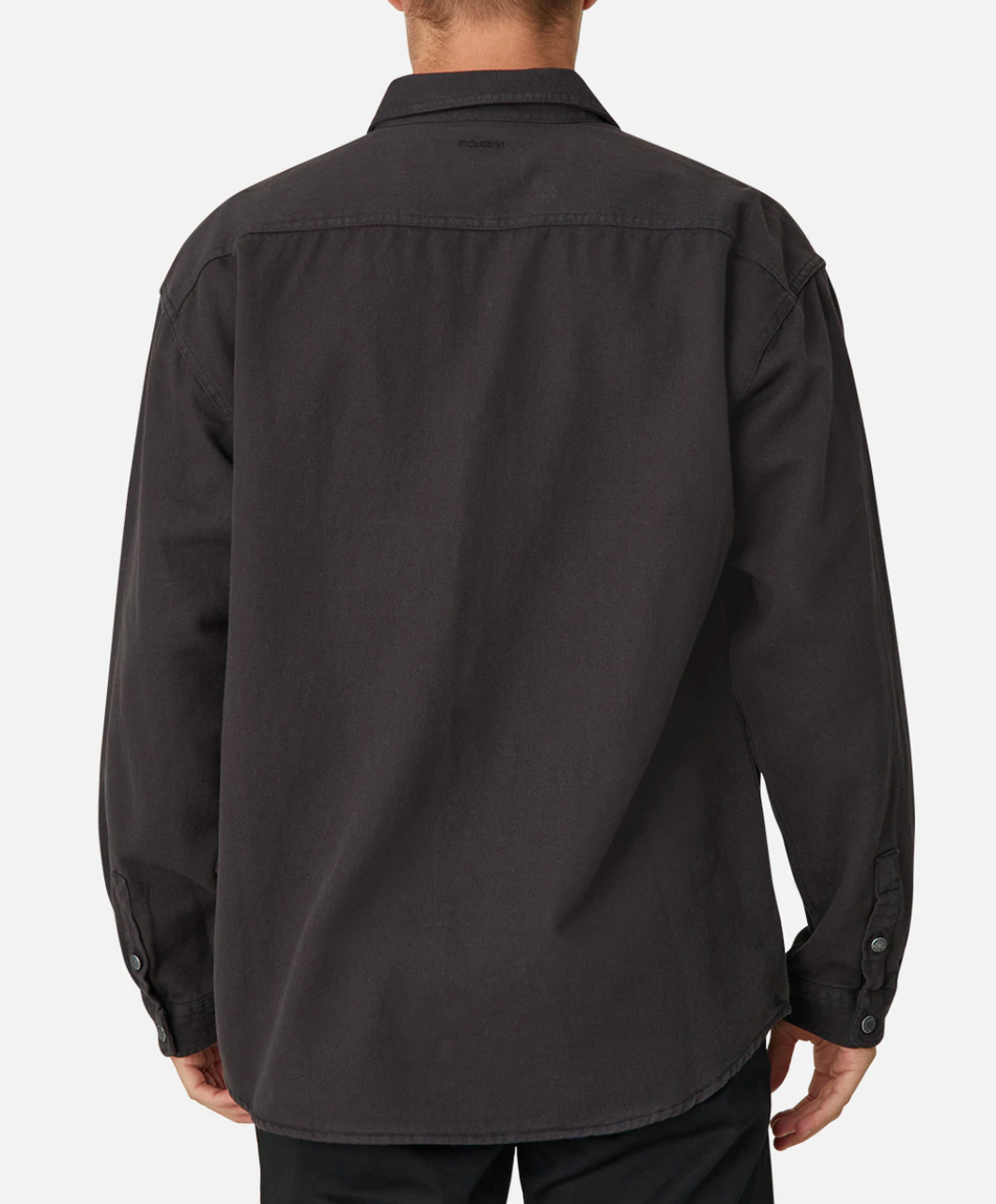 A person wearing the Industrie The Portland Shirt, a stylish, long-sleeved black button-up crafted from a cotton/linen blend, stands facing away from the camera against a plain white background. The shirt features an Industrie logo on the collar, buttoned cuffs, and a slightly curved hem.