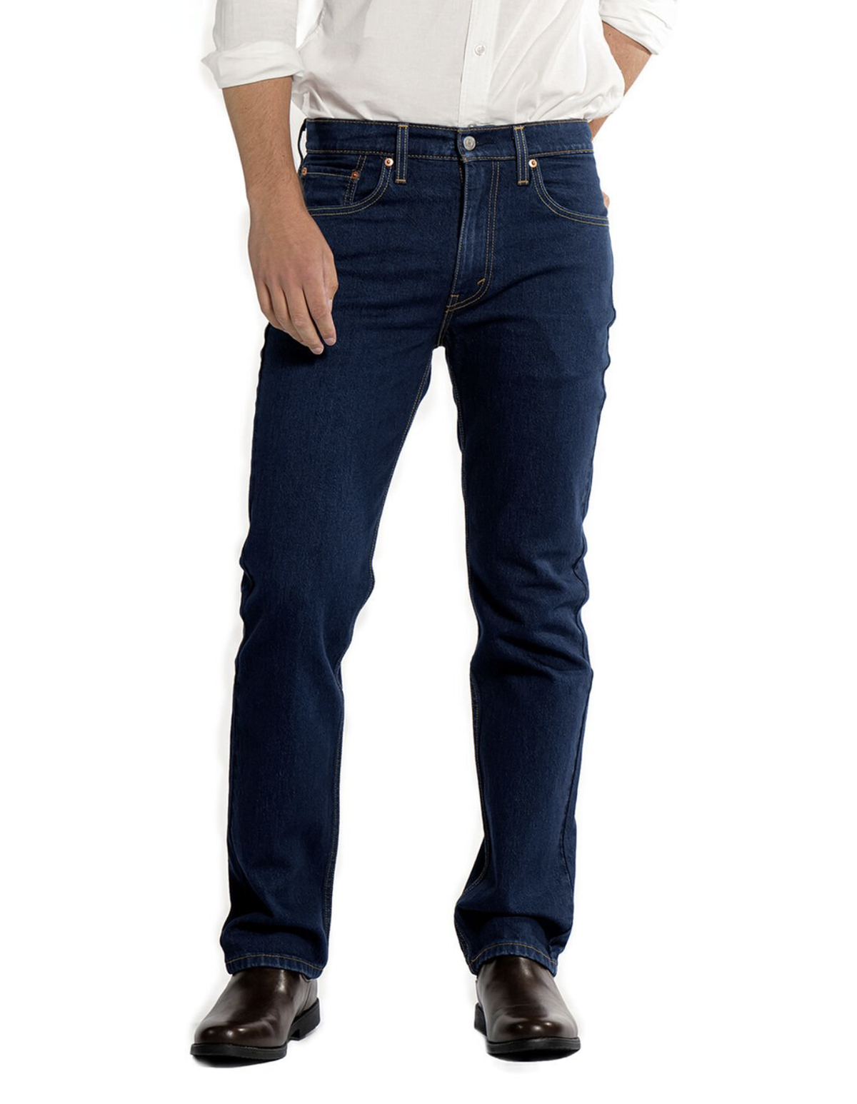 A person standing against a white background, wearing a white long-sleeve button-up shirt, dark blue Levis 516 Straight Jean with visible stitching around the pockets and seams, paired with dark brown boots.