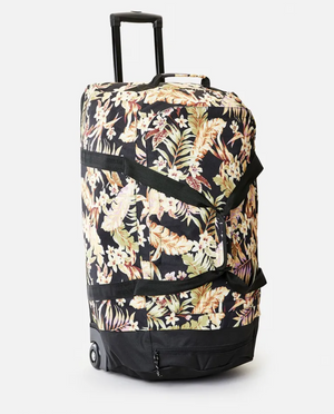 The Rip Curl Jupiter 80L Sunday Swell Travel Bag showcases a vibrant tropical floral design on black, crafted from recycled polyester. It includes a telescopic handle, two durable black wheels, and sleek black front straps.