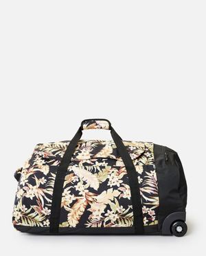 The Rip Curl Jupiter 80L Sunday Swell Travel Bag is a black wheeled duffel with a vibrant floral print of beige and white flowers and green leaves. Made from recycled polyester, it includes sturdy black handles and a side zipper pocket.