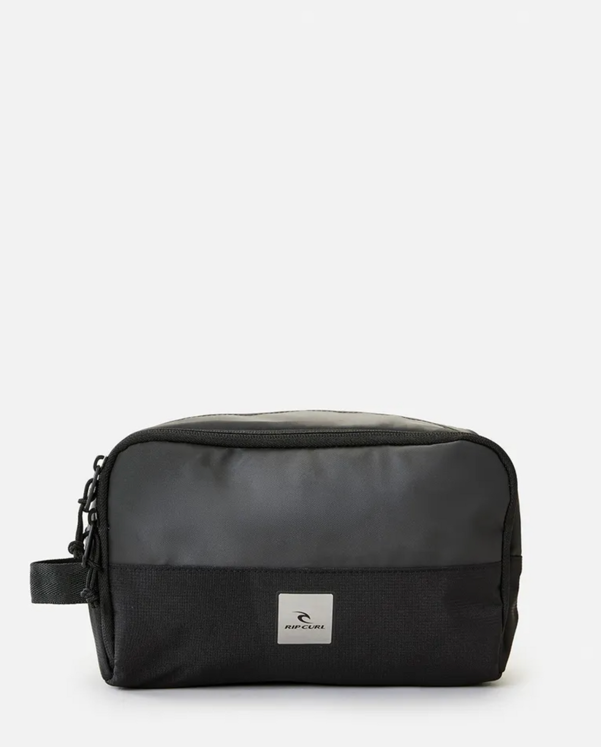 The Rip Curl Groom Toiletry Midnight, a rectangular black polyester bag, is displayed against a plain white background. It has a strap on the left side and features a small rectangular patch on the front with the Rip Curl logo of a bird in flight and text beneath it. The bag boasts a sleek, minimalist design.