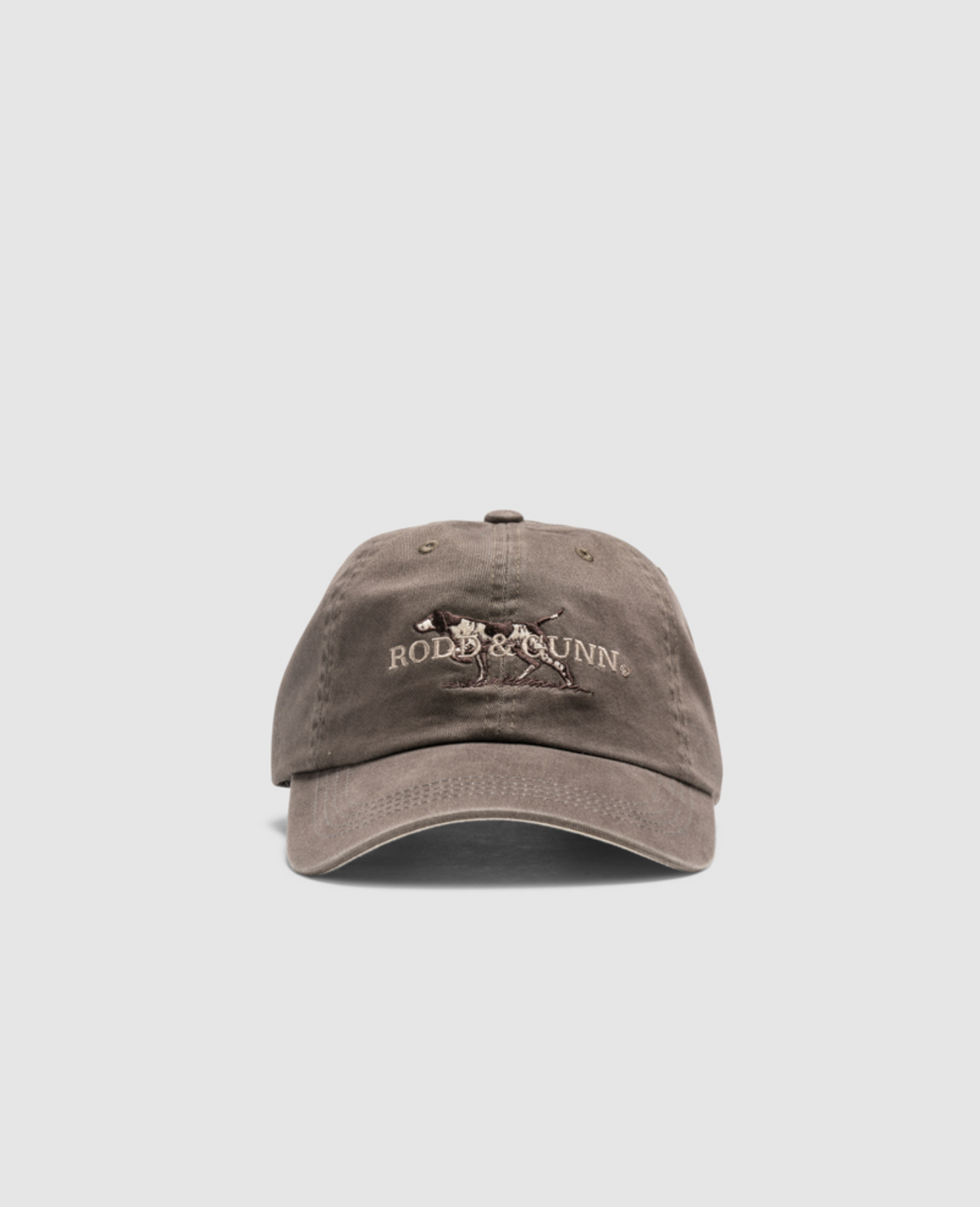 The Rodd & Gunn Double Barrel Cap is a brown hat featuring the Rod & Gunn logo embroidered on the front, which showcases a dog above the name "Rod & Gunn" in white text. Crafted from heavy-duty cotton twill, this cap includes a curved brim, six-panel construction, and an adjustable strap.