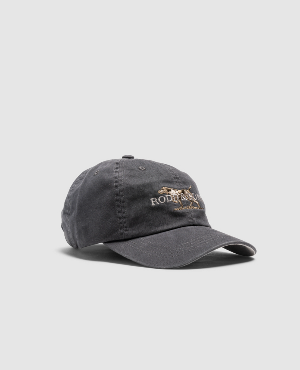 The Rodd & Gunn Double Barrel Cap is a dark gray heavy-duty cotton twill cap, featuring an embroidered rodeo scene on the front. It's slightly worn and showcased against a light gray background.