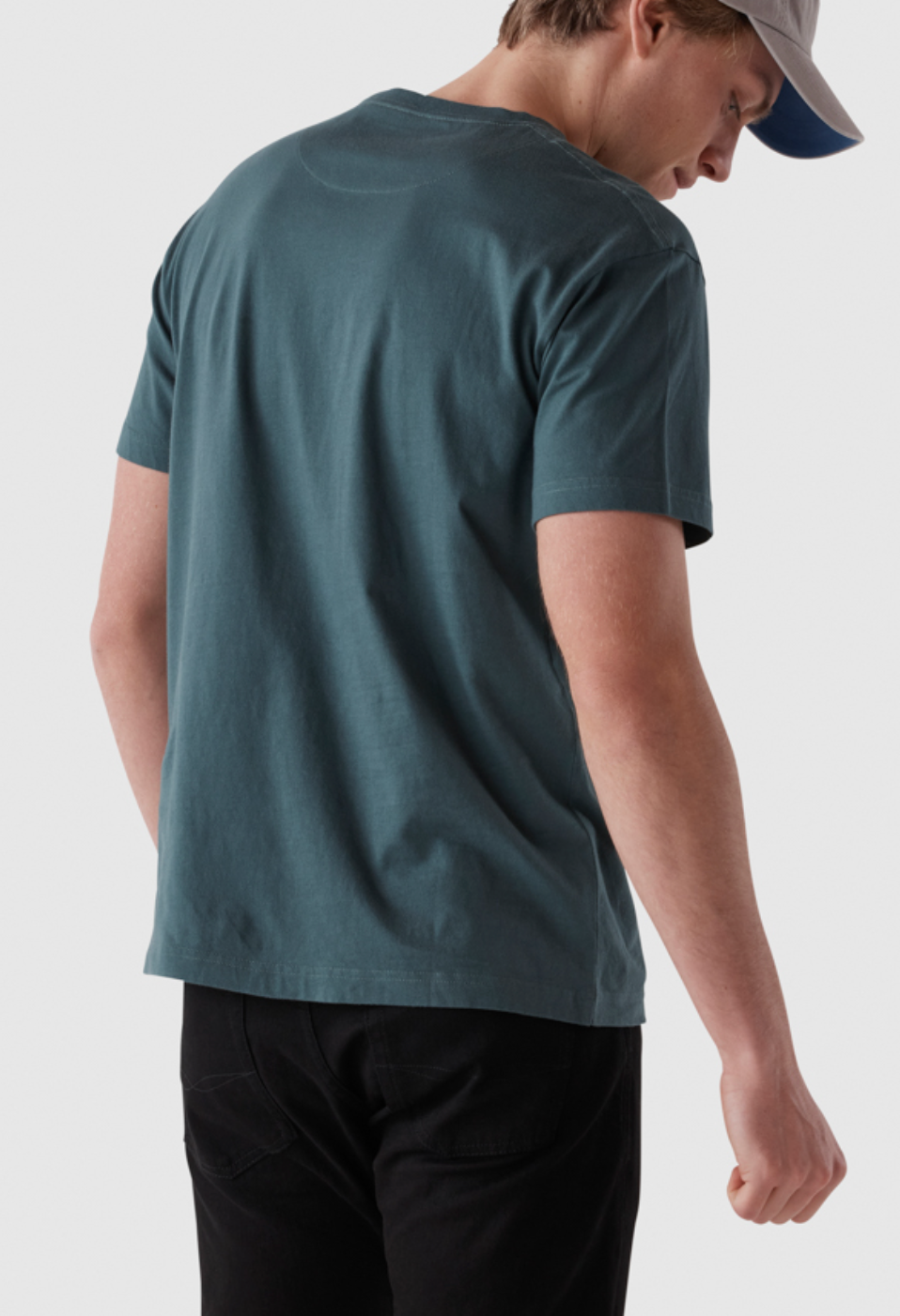 A person in a Rodd & Gunn The Gunn T-Shirt, made from Australian cotton in sports fit, paired with black pants and a light gray cap, is standing against a plain background. Captured from behind, the image emphasizes the comfort of the tee.