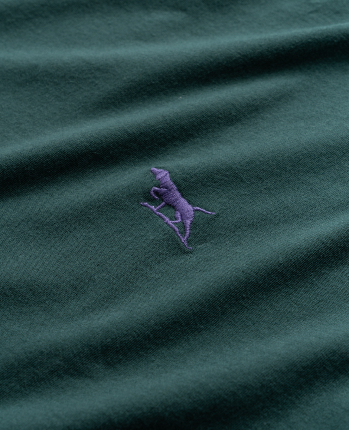 The Rodd & Gunn The Gunn T-Shirt in dark green, made from premium Australian Cotton, showcases a purple embroidered logo of a walking dog or horse. Its comfortable sports fit merges casual style with understated elegance.