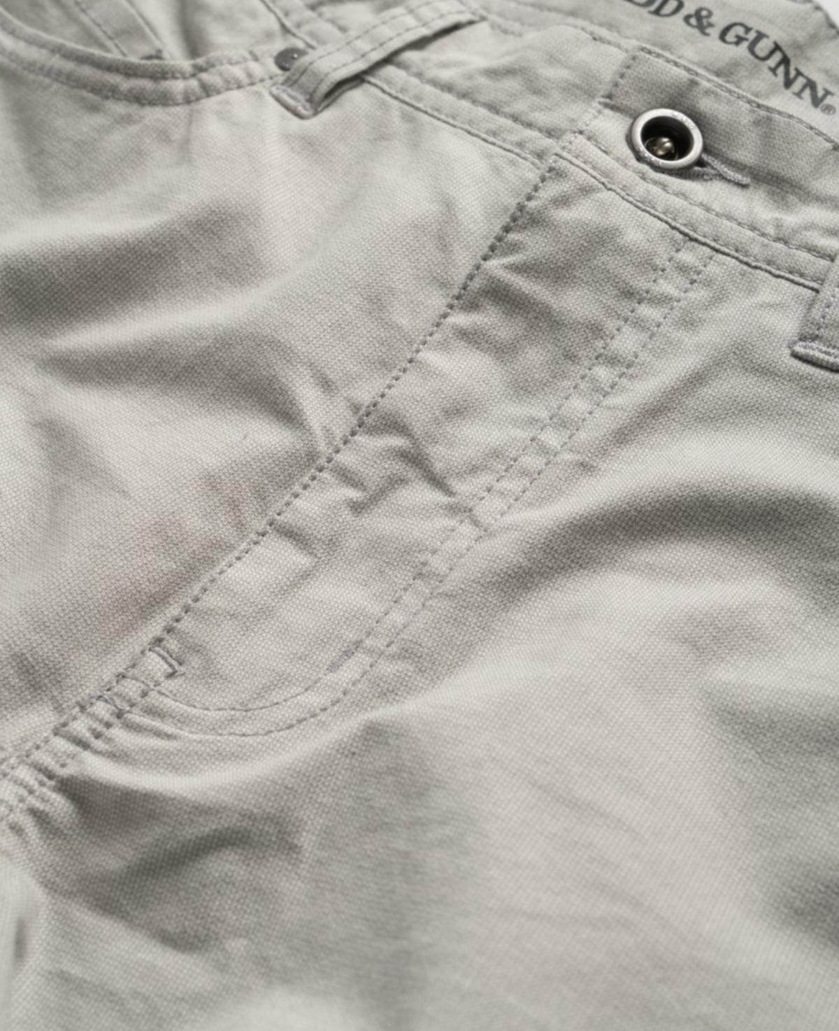 Close-up of Rodd & Gunn Straight Fit Jean in light grey, highlighting the front pocket area. The stitching detail and metal rivets are visible, giving a casual and durable appearance. The stretch fabric enhances comfort, and the texture of the material suggests a cotton blend. YKK zip fly adds to its durability.