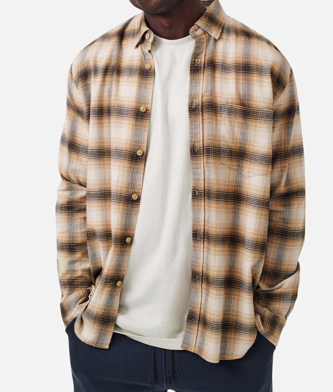 The image displays a person wearing a comfy, 100% cotton white tee under an unbuttoned Industrie The Bates Shirt featuring beige, black, and brown plaid. They also have dark pants on against a plain white background, with their face not visible.